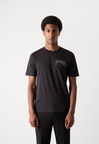 Black cotton t-shirt featuring a crew neck and short sleeves. Notable logo in contrasting color on the left chest. Smooth texture.
