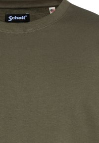 Camiseta de cuello redondo acanalada en verde oliva, fabricada con mezcla de algodón, con etiqueta visible cerca del cuello que muestra el logo de Schott.