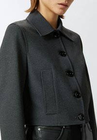 Giacca grigia corta realizzata in tessuto testurizzato, con colletto a punta, cinque bottoni neri e una tasca laterale.