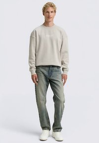 Gaiši pelēks džemperis ar apaļu kakla izgriezumu, kombinēts ar izbalējušām zilām džinsām un baltām sporta kurpēm. Ikdienišķa piegriezuma džemperis ar ribveida aprocēm un apakšu.