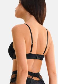 Soutien-gorge noir avec des panneaux en dentelle transparente, des straps réglables, une fermeture par crochet et œillet, et des détails de broderie florale. Texture de tissu lisse.