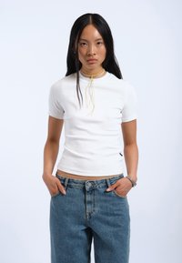 Hvid, tætsiddende kortærmet t-shirt med høj halsudskæring. Sammen med løse, mellemblå denimjeans. Enkel design uden synlige mønstre.