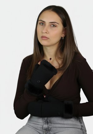 Guantes negros sin dedos con puños de felpa y detalle de botón, hechos de una tela suave, combinados con un top ajustado y vaqueros.