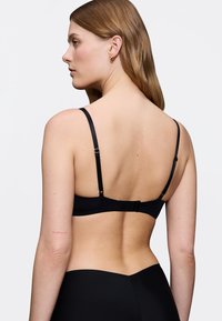 Reggiseno nero con ferretto, spalline regolabili, texture liscia e chiusura a gancio e occhiello sul retro, abbinato a slip a vita alta tono su tono.