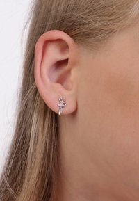 Silberne Balletttänzer-Ohrringe mit einem rosa Akzent und klaren Edelsteindetails, präsentiert am Ohr eines Modells mit heller Haut und Haar.