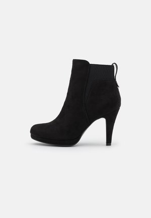 Bottes de cheville en daim noir avec un bout pointu, un talon aiguille haut et des panneaux latéraux élastiques. Elles comportent une languette à l'arrière pour un enfilage facile.