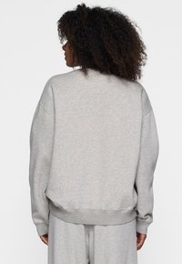 Grauer Sweatshirt mit lockerer Passform, weiten Ärmeln, einem gerippten Saum und einem weichen, strukturierten Stoff. Einfaches Design ohne Verzierungen.