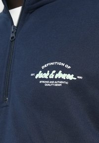 Φούτερ μπλε ναυτικού με φερμουάρ, με λεία υφή, διακοσμημένο με λευκό και ανοιχτό πράσινο τυπωμένο κείμενο και λαιμό με φερμουάρ.