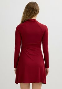 Vestido rojo de manga larga con un cuerpo ajustado y falda acampanada. Textura suave, escote alto y diseño de espalda sin costuras.