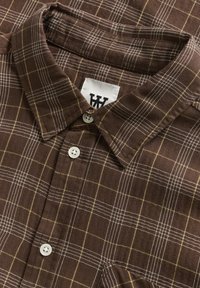 Chemise marron à motif avec un design à carreaux, ornée de lignes jaunes et blanches, en tissu texturé, avec un col classique et une fermeture à bouton.