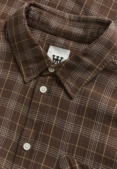 Chemise marron à motif avec un design à carreaux, ornée de lignes jaunes et blanches, en tissu texturé, avec un col classique et une fermeture à bouton.
