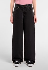 Black wide-leg jeans made of denim, featuring a high waist, front pockets, and subtle textured finish. Paired with black sneakers.