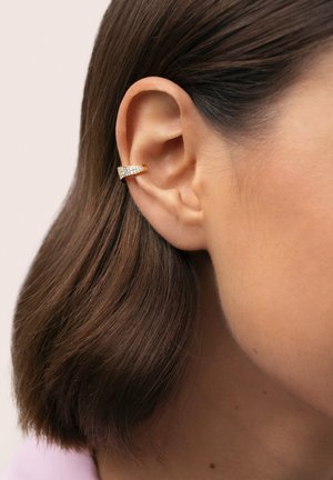 Pendiente de oreja de oro con un diseño curvo elegante adornado con pequeñas gemas transparentes, sobre cabello corto y castaño y un fondo neutro.