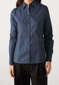 Camicia button-up blu navy con colletto, maniche lunghe e taglio dritto. Presenta bottoni coordinati e una finitura in tessuto liscia.