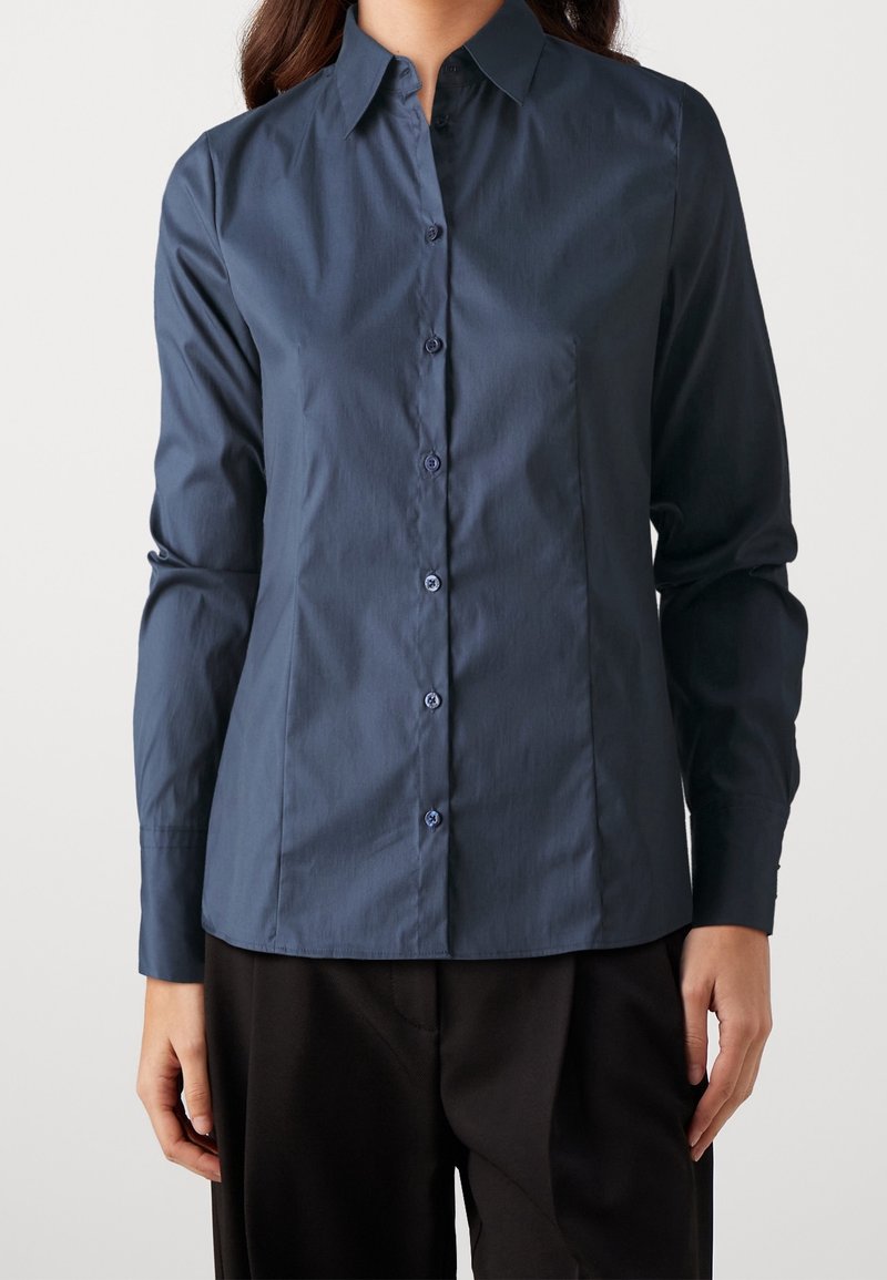 Camicia button-up blu navy con colletto, maniche lunghe e taglio dritto. Presenta bottoni coordinati e una finitura in tessuto liscia.