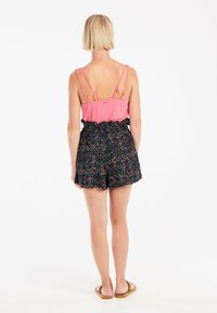 Débardeur rose à fines bretelles, associé à un short noir avec un motif floral et un ourlet à volants, porté avec des sandales beiges.