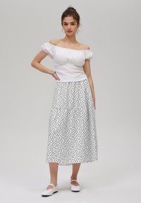 White off-the-shoulder top with textured design paired with a mid-length skirt featuring black polka dots and white flats.