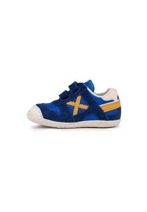 Zapatilla infantil de ante azul y marino con tiras de Velcro, suela de goma blanca y acentos amarillos, que presenta un patrón en cruz en el lateral.