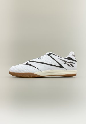 Witte en zwarte lage Reebok sportschoen met rubberen zool, zijlogo en gestikte details op een neutrale achtergrond.