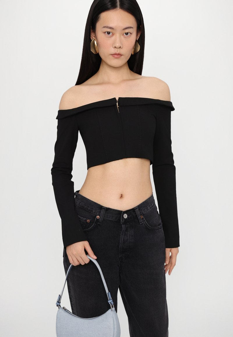 Haut court noir à épaules dénudées avec des manches longues et une fermeture éclair à l'avant ; associé à un jean foncé taille haute et un sac bleu clair.