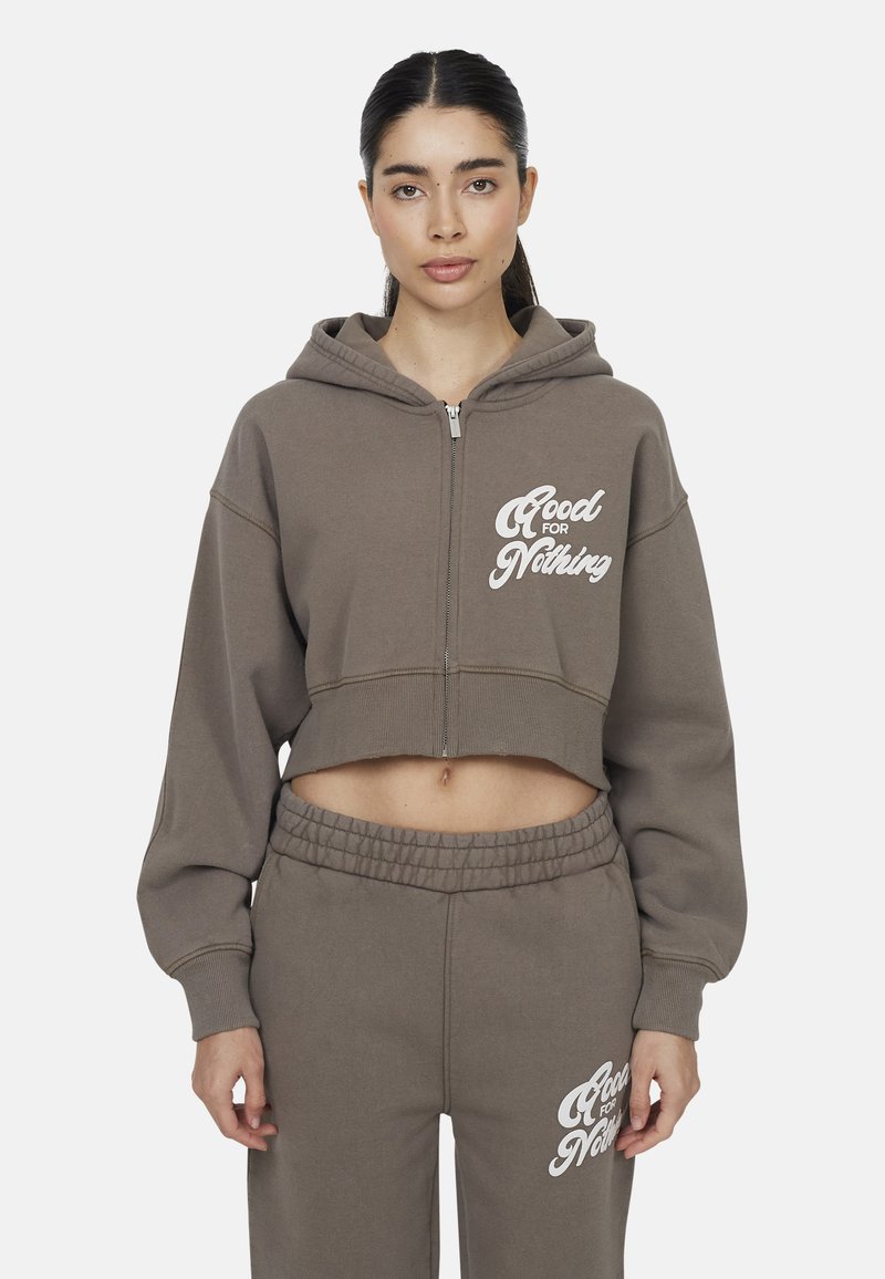 Felpa taupe tagliata con testo bianco "Good for Nothing", dotata di zip e cappuccio con cordino; abbinata a pantaloni felpati a sigaretta coordinati.