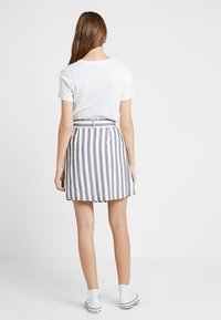 Grå och vit randig kjol med bälte i midjan, ovanför knäet, kombinerad med en enkel vit t-shirt och vita sneakers.