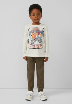 Witte lange mouwen overhemd met een circus tijger grafiek, gecombineerd met bruine broek met zijstreepjes en witte sportieve schoenen.