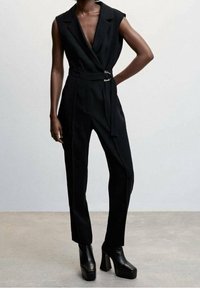 Black sleeveless jumpsuit with a deep v-neck, belted waist, and wide-leg design. Fabric appears smooth with a tailored fit.