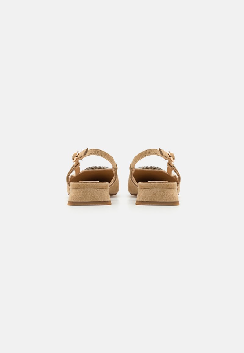 Sandalias de ante en color marrón con correas alrededor del tobillo, tacones cuadrados bajos y acentos decorativos en la parte trasera. Textura suave con un diseño simple y limpio.