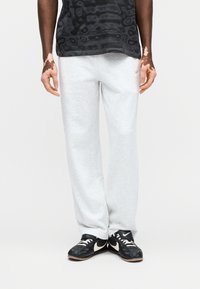 Γκρι βαμβακερές φόρμες με άνετη εφαρμογή, με απλό σχέδιο και μικρό λογότυπο. Συνδυασμένες με μαύρα αθλητικά παπούτσια με λευκές λεπτομέρειες.