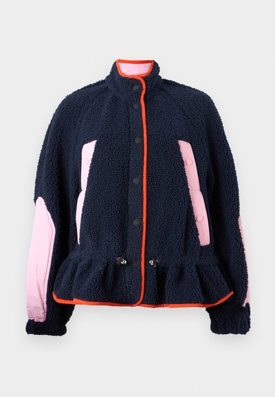 Fleece jakna z mornarsko modrim telesom, rožnatimi stranskimi paneli in oranžnimi obrobami. Ima visok ovratnik in nabran rob, z črnimi gumbi.
