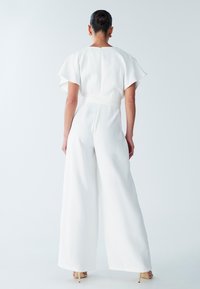 Witte jumpsuit met een wijde pijp, korte uitlopende mouwen en een taille met ceintuur. Gladde textuur en minimalistische stijl.