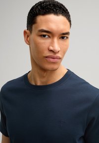 Czarnoniebieska koszulka bawełniana z okrągłym dekoltem, krótkimi rękawami i małym wyszywanym logo na klatce piersiowej. Miękka faktura.