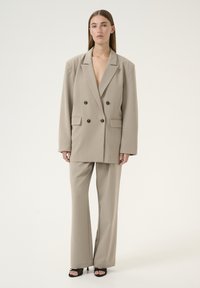 Beige Doppelreiher-Blazer mit schwarzen Knöpfen, kombiniert mit passenden taillierten Hosen. Glatte Textur, übergroße Silhouette und minimalistisches Design.