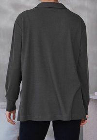 Chemise à manches longues gris foncé, côtelée, avec col, offrant une coupe décontractée et des fentes sur les côtés à l'ourlet pour faciliter les mouvements.