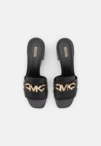 Black leather slide sandals featuring a wide strap with a gold-tone "MK" logo, low block heel, and smooth texture.