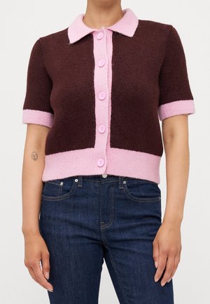 Cardigan marron à manches courtes avec col rose, patte de boutonnage, poignets et ourlet, porté avec un jean bleu foncé.