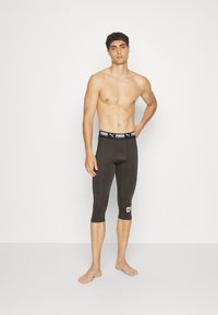 Fekete sport leggings, testhez simuló fazonnal, térdhez érő hosszúsággal és logós, rugalmas derékkal. Simább textúra és minimális részletesség.