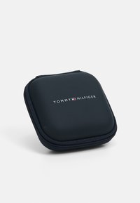 Mustas kinnitusketiga kõvakarp, millel on ümar ruudukujuline kuju. Omab valget "TOMMY HILFIGER" logo väikese värvilise embleemiga.