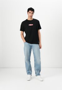 Black cotton t-shirt with red "GUESS JEANS" logo. Worn with light blue distressed jeans and white sneakers. Simple, casual design.