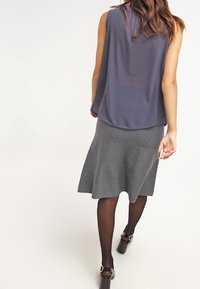 Canotta grigia senza maniche con un design fluido, abbinata a una gonna grigia al ginocchio. Modella con tacchi neri. Tessuto e silhouette lisci.
