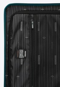 Černý textilní interiér kufru s síťovou kapsou, vodorovnými pruhy a potištěnými grafikami letadel. Obsahuje štítek s pokyny k údržbě.