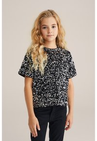 Mustat lyhythihaiset paidat, jotka on päällystetty hopeisilla paljeteilla; niissä on pyöreä kaula-aukko ja löysä malli, yhdistettynä mustiin housuihin.