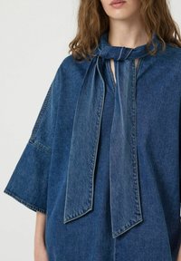 Top de denim con detalle de lazo en el cuello, mangas amplias y corte relajado. Color azul oscuro con una textura suave y sutilezas en las costuras.