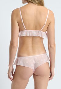Conjunto de lencería rosa transparente con bordados florales, bordes con volantes, tirantes ajustables y una textura suave. El diseño incluye una parte inferior a juego.
