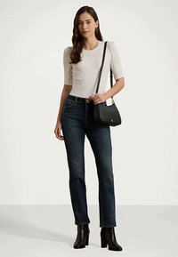 Top curto de manga curta ribbed branco, jeans azul escuro, carteira preta com metalizado dourado e botas pretas de salto. Modelo de pé contra um fundo claro.