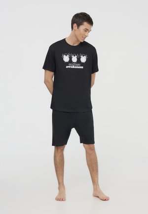 Set di t-shirt nera e pantaloni corti realizzato in tessuto morbido. La t-shirt presenta una grafica di orologi con il testo "risveglio infinito". Design semplice.