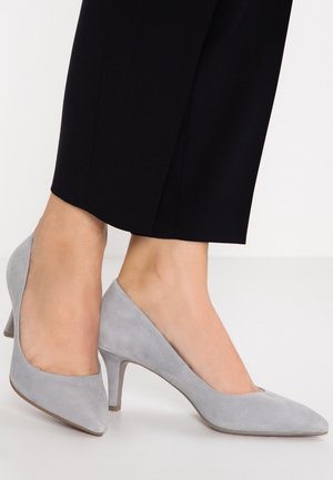 Gray suede high-heeled shoes with a pointed toe and a mid-height heel. The shoes feature a smooth texture and calf-length black pants.