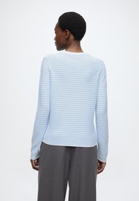 Hele sinised triibulised pika varrukaga pluus ümarate kaelustega ja soonilise tekstuuriga, kombineeritud hallide laiade pükstega.