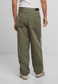 Pantalones de pierna ancha verde oliva hechos de algodón, con dos bolsillos traseros y una cinturilla con etiqueta. Material texturizado con un acabado suave.